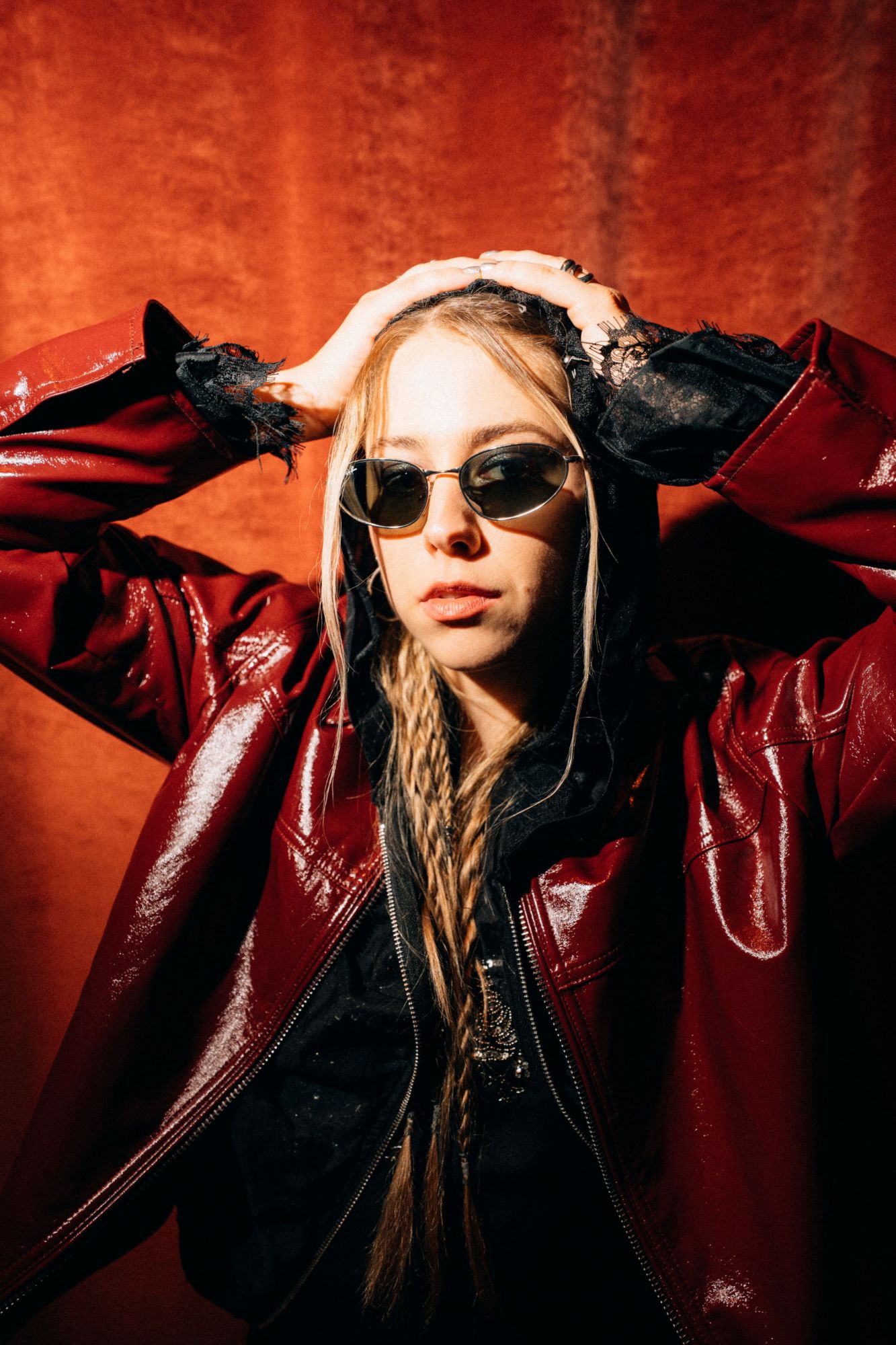 Selbstbewusstes Studioportrait in roter Lederjacke mit Sonnenbrille vor warmem Rotlicht-Hintergrund